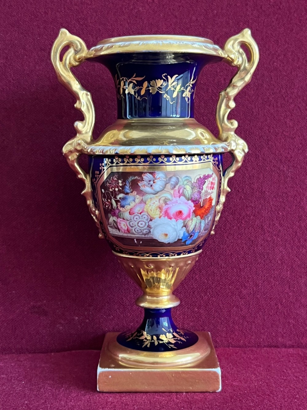 A three-piece set of cobalt blue and gilded Minton porcelain urn vases featuring hand-painted floral panels on square plinths. View V