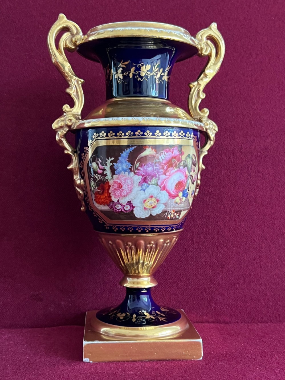 A three-piece set of cobalt blue and gilded Minton porcelain urn vases featuring hand-painted floral panels on square plinths. View VI