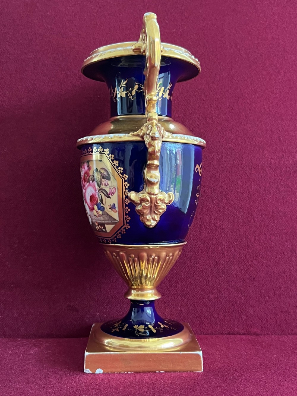 A three-piece set of cobalt blue and gilded Minton porcelain urn vases featuring hand-painted floral panels on square plinths. View VII
