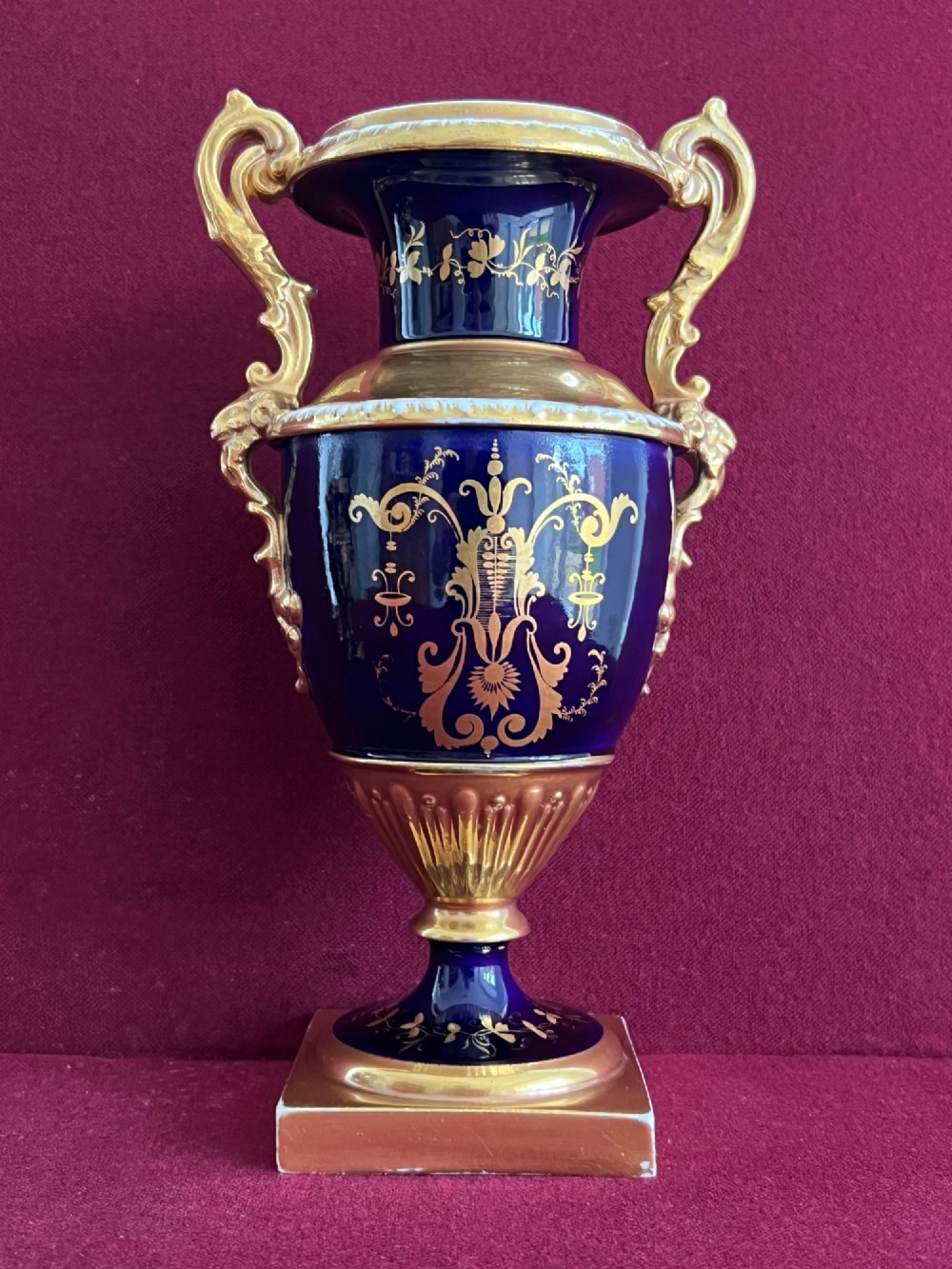 A three-piece set of cobalt blue and gilded Minton porcelain urn vases featuring hand-painted floral panels on square plinths. View VIII