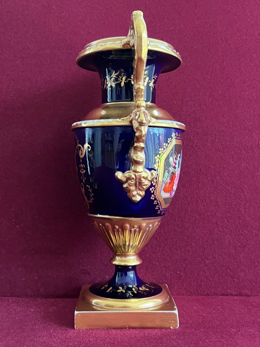 A three-piece set of cobalt blue and gilded Minton porcelain urn vases featuring hand-painted floral panels on square plinths. View IX