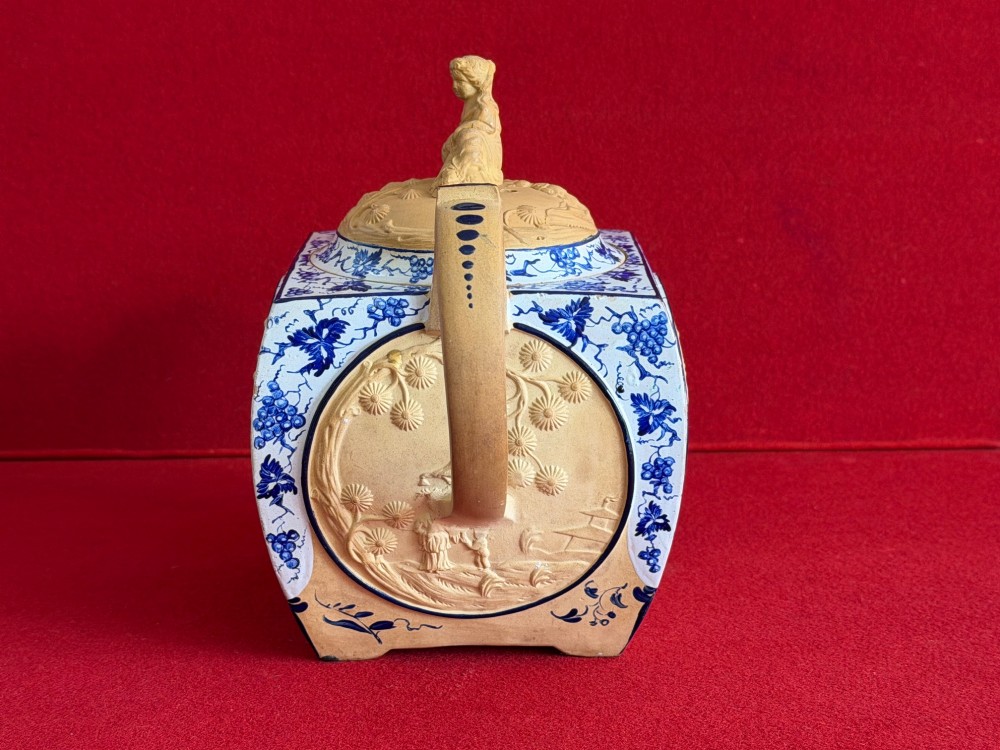 An eighteenth-century box-shaped Spode caneware teapot with moulded Chinoiserie relief panels, blue foliage borders, and a reclining figural lid finial. View IV