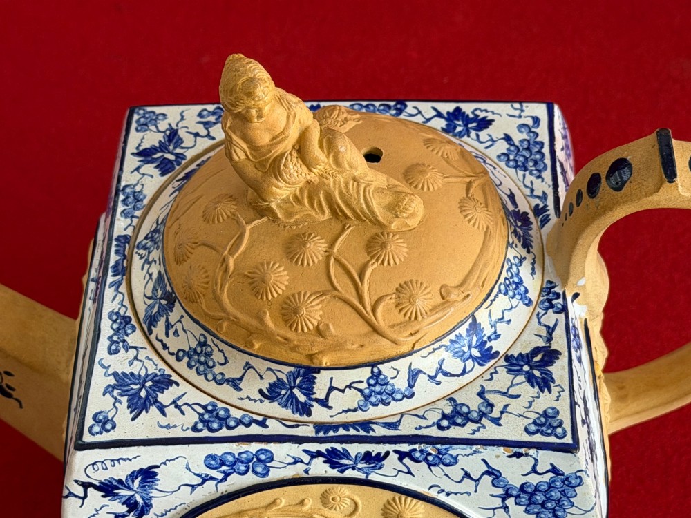 An eighteenth-century box-shaped Spode caneware teapot with moulded Chinoiserie relief panels, blue foliage borders, and a reclining figural lid finial. View V