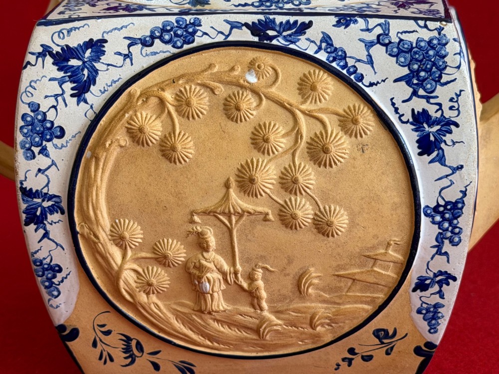 An eighteenth-century box-shaped Spode caneware teapot with moulded Chinoiserie relief panels, blue foliage borders, and a reclining figural lid finial. View VII