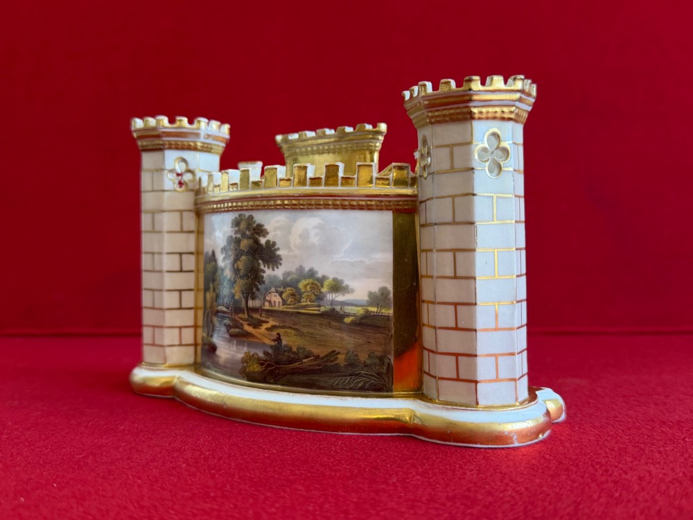 An English porcelain spill vase in the form of a castle with gilded turrets, crenellated rims, and a central painted landscape panel. View V