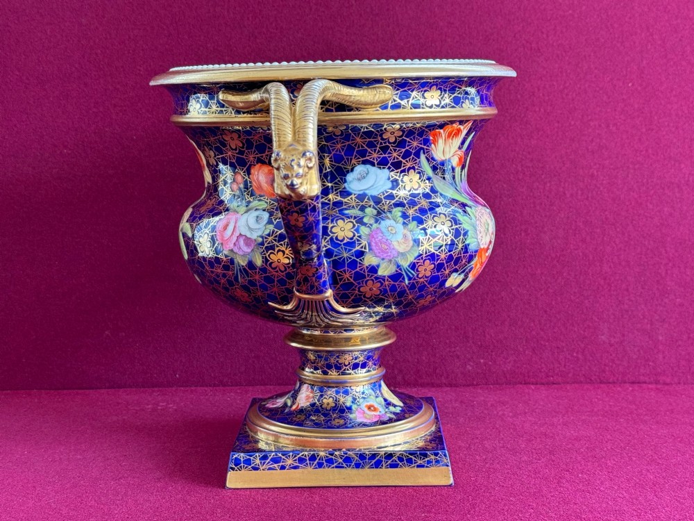 An English Regency porcelain Warwick vase featuring a deep cobalt blue ground with a gilt lattice pattern, twin handles, and a central reserve painted with colourful flowers. View II