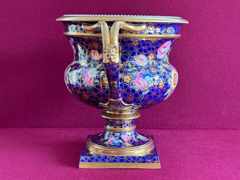 An English Regency porcelain Warwick vase featuring a deep cobalt blue ground with a gilt lattice pattern, twin handles, and a central reserve painted with colourful flowers. View IV