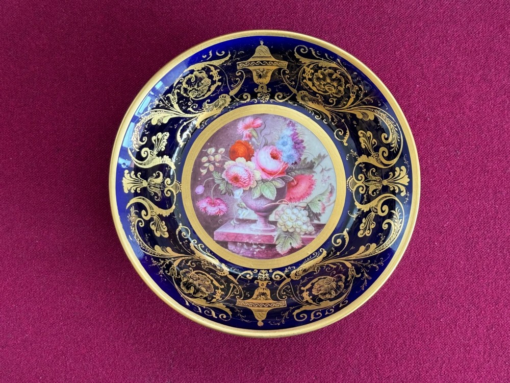 A cylindrical porcelain coffee can and saucer featuring deep cobalt blue grounds, elaborate gilt scrollwork, and central hand-painted floral still-life panels. View III