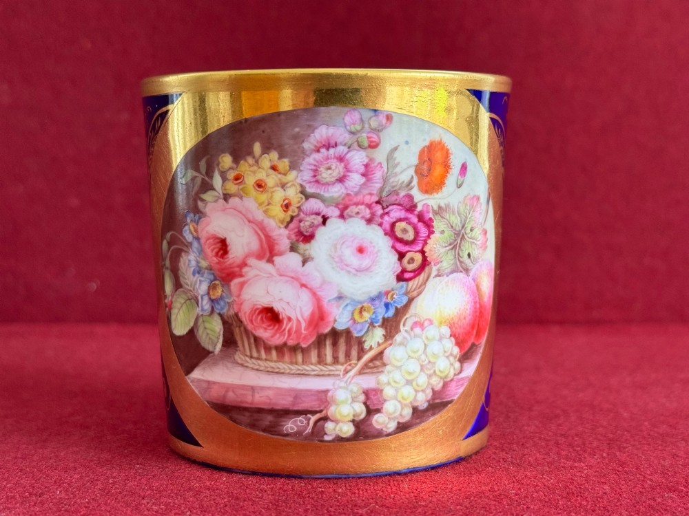 A cylindrical porcelain coffee can and saucer featuring deep cobalt blue grounds, elaborate gilt scrollwork, and central hand-painted floral still-life panels. View IV
