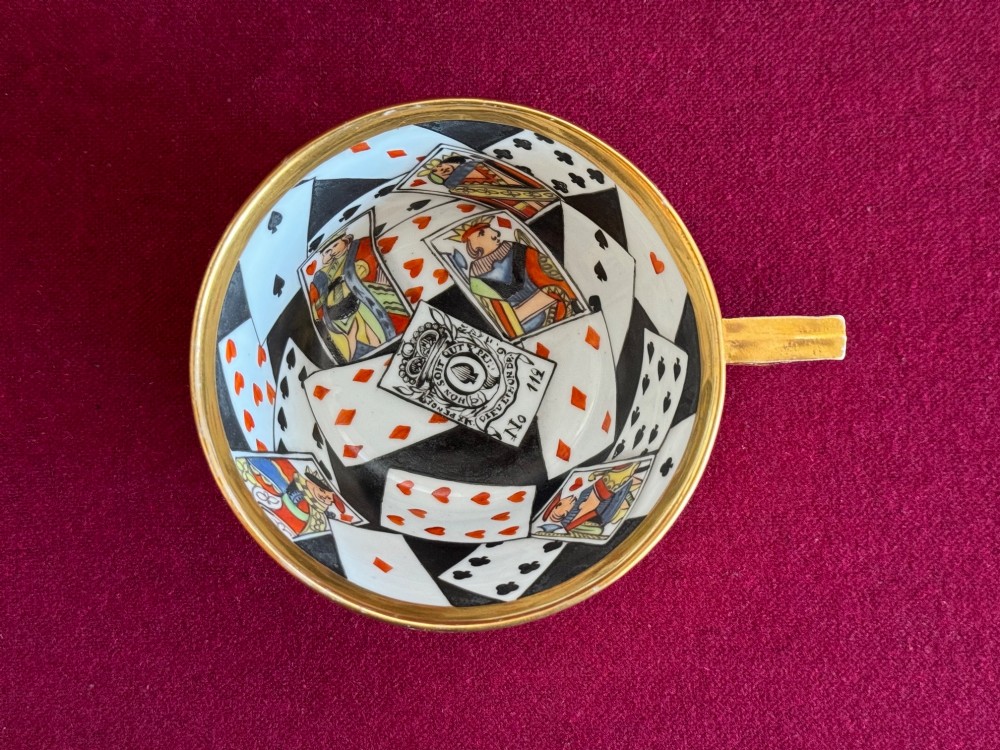 An antique porcelain teacup and saucer featuring a gilded exterior and a detailed hand-painted playing card pattern on the interior surfaces. View II