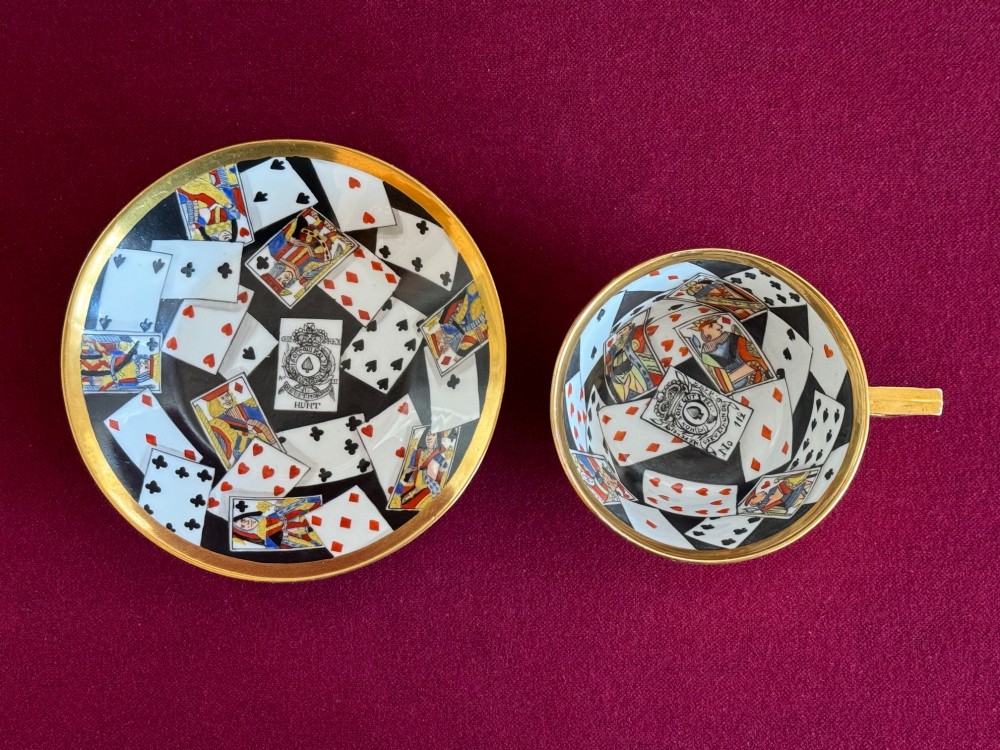 An antique porcelain teacup and saucer featuring a gilded exterior and a detailed hand-painted playing card pattern on the interior surfaces. View IV