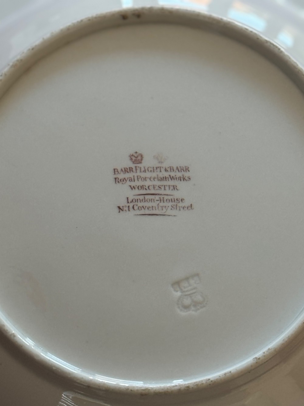 A circular Regency porcelain soup plate featuring a central heraldic crest, surrounded by a faux-marble ground and a broad gilded rim. View III