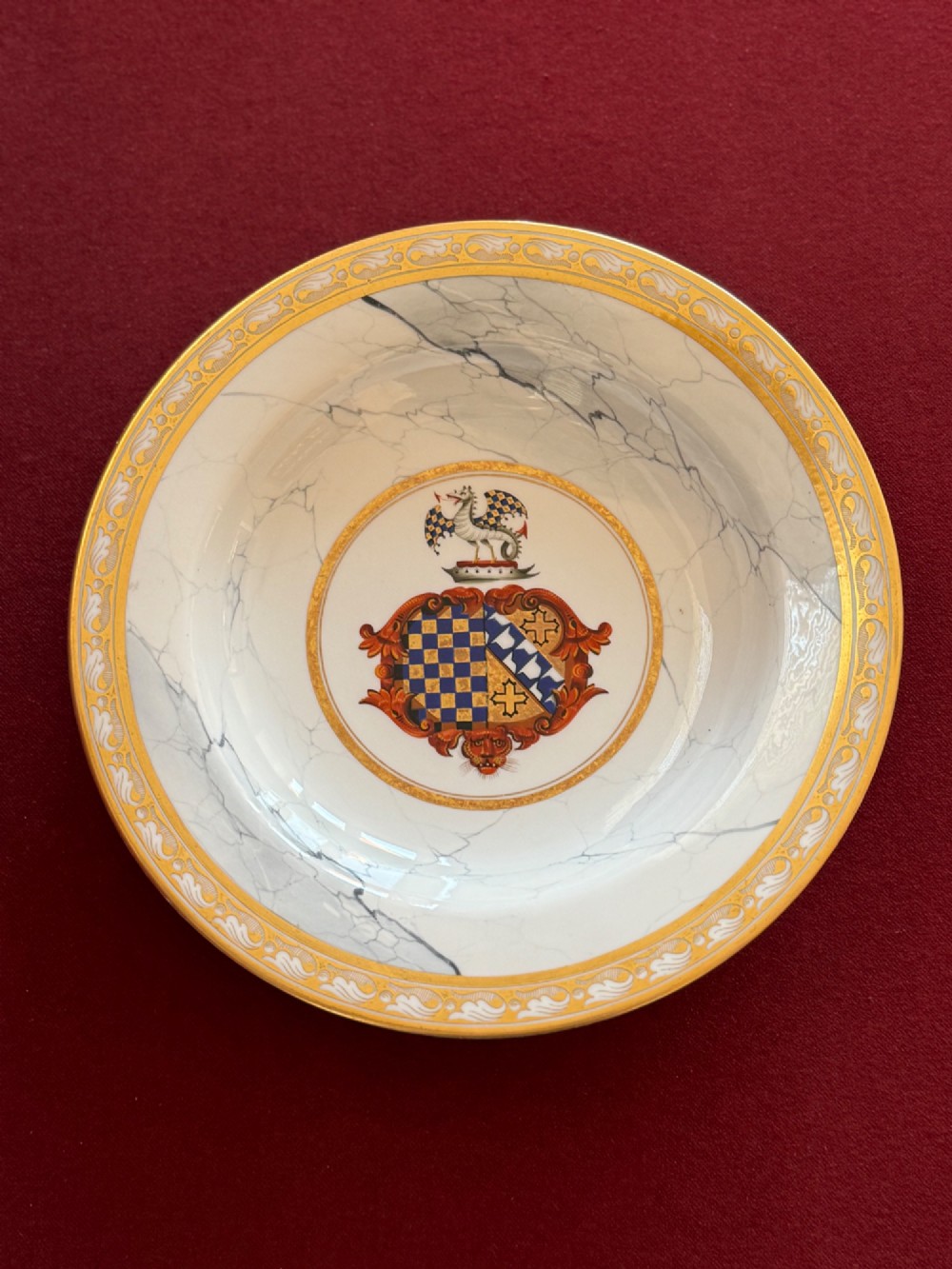 A circular Regency porcelain soup plate featuring a central heraldic crest, surrounded by a faux-marble ground and a broad gilded rim. View IV