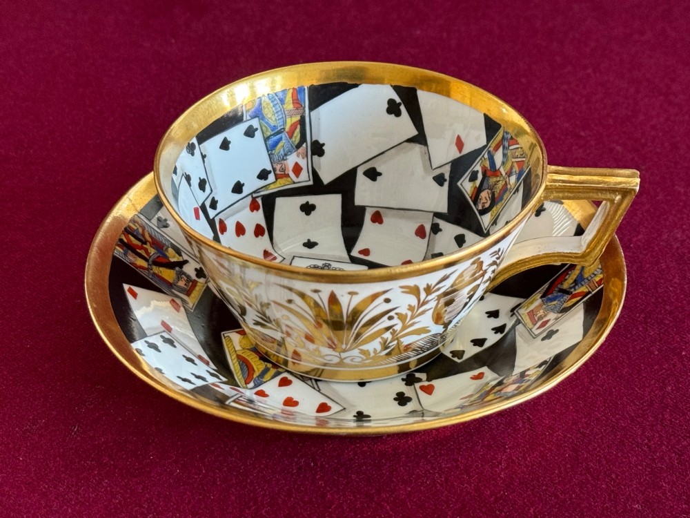 An early nineteenth-century porcelain teacup decorated with terracotta classical foliage alongside a saucer painted with a trompe loeil playing card pattern. View V