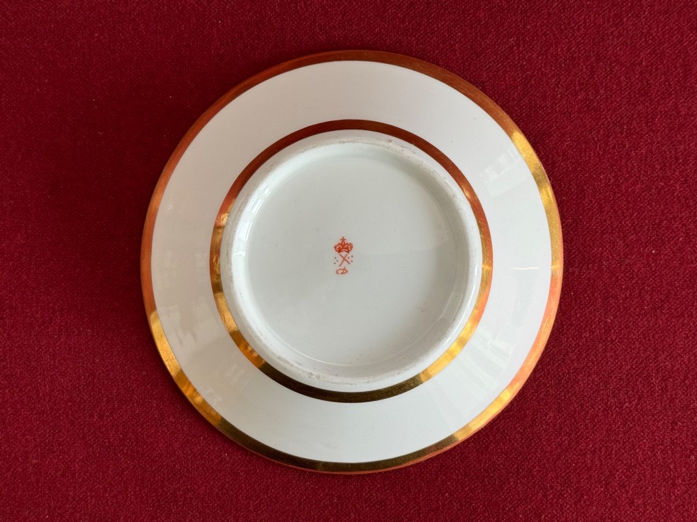 An early nineteenth-century porcelain teacup decorated with terracotta classical foliage alongside a saucer painted with a trompe loeil playing card pattern. View VI