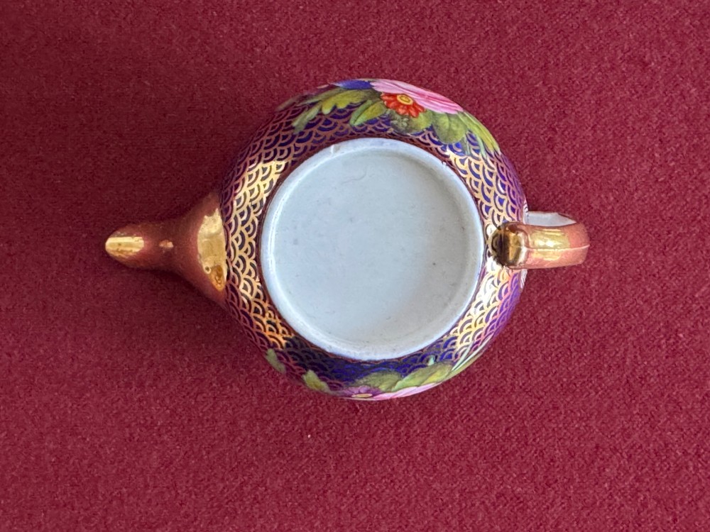 An antique Regency period miniature porcelain teapot decorated with intricate gold scale patterns on dark blue porcelain and hand-painted floral panels. View III