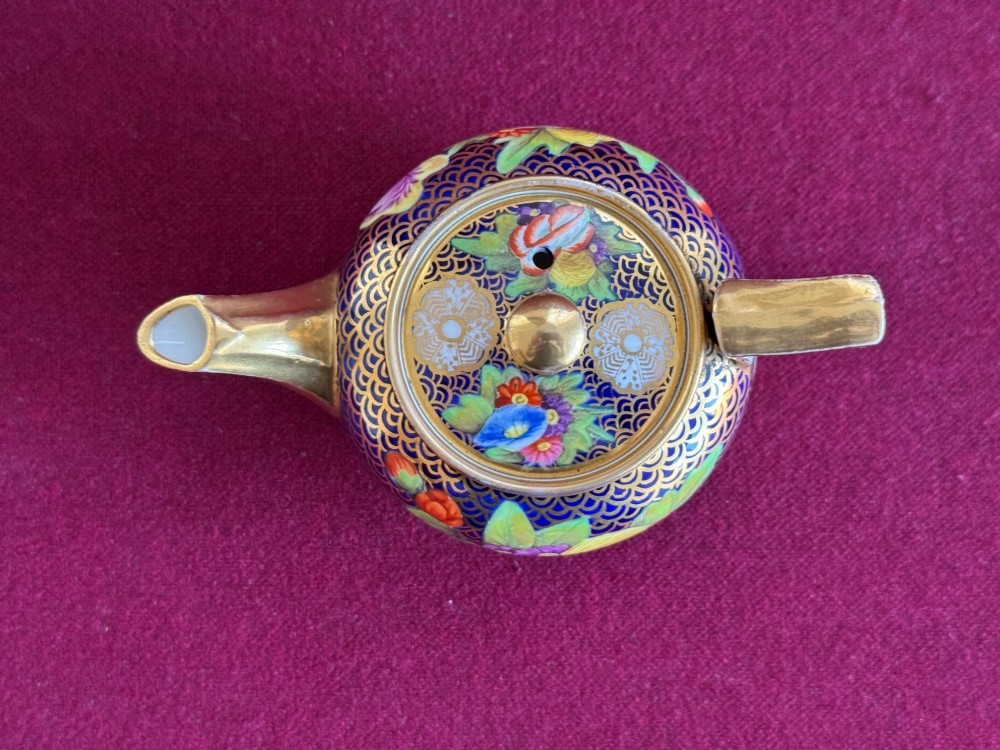 An antique Regency period miniature porcelain teapot decorated with intricate gold scale patterns on dark blue porcelain and hand-painted floral panels. View IV