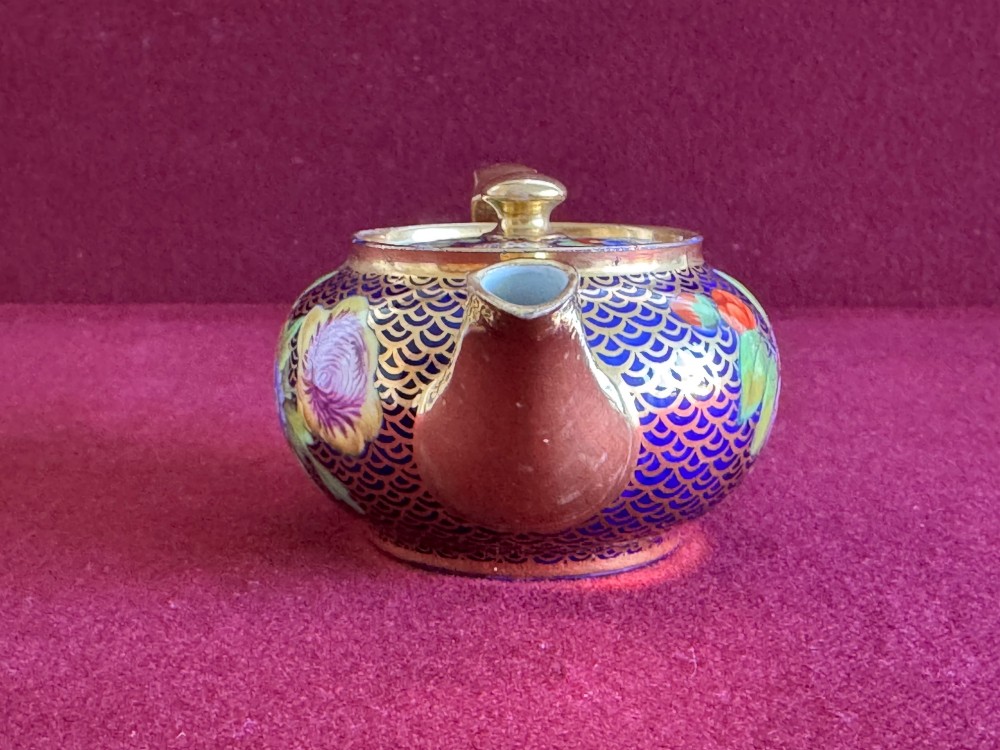 An antique Regency period miniature porcelain teapot decorated with intricate gold scale patterns on dark blue porcelain and hand-painted floral panels. View V