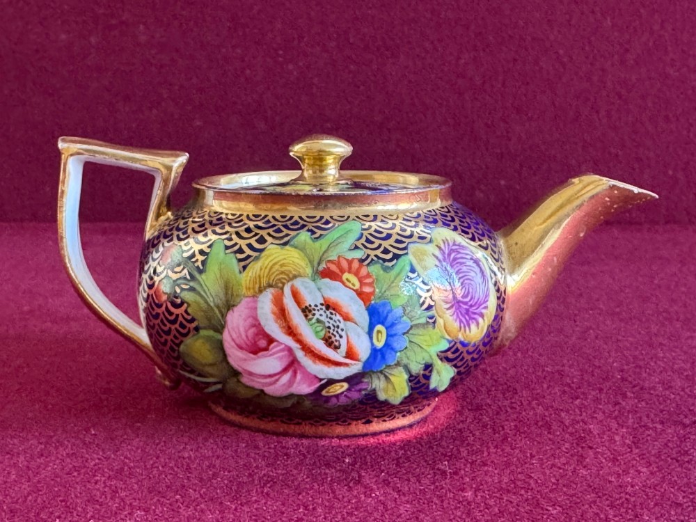 An antique Regency period miniature porcelain teapot decorated with intricate gold scale patterns on dark blue porcelain and hand-painted floral panels. View VII