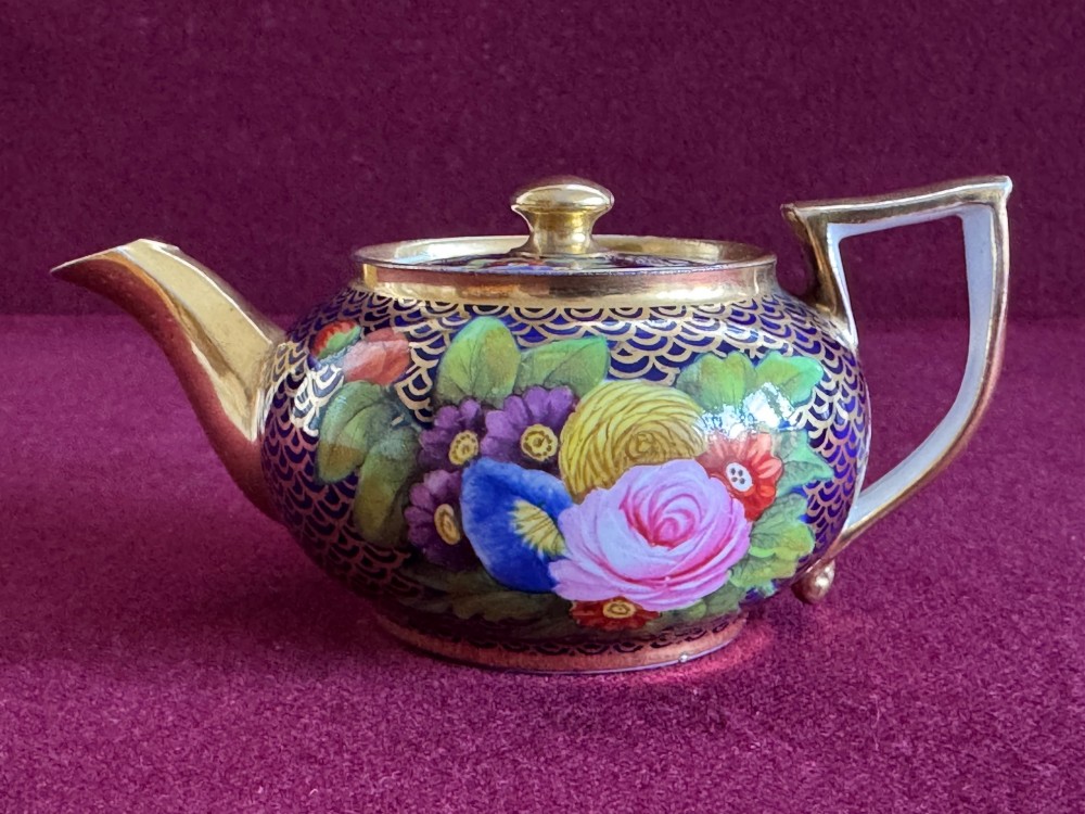 An antique Regency period miniature porcelain teapot decorated with intricate gold scale patterns on dark blue porcelain and hand-painted floral panels. View VIII