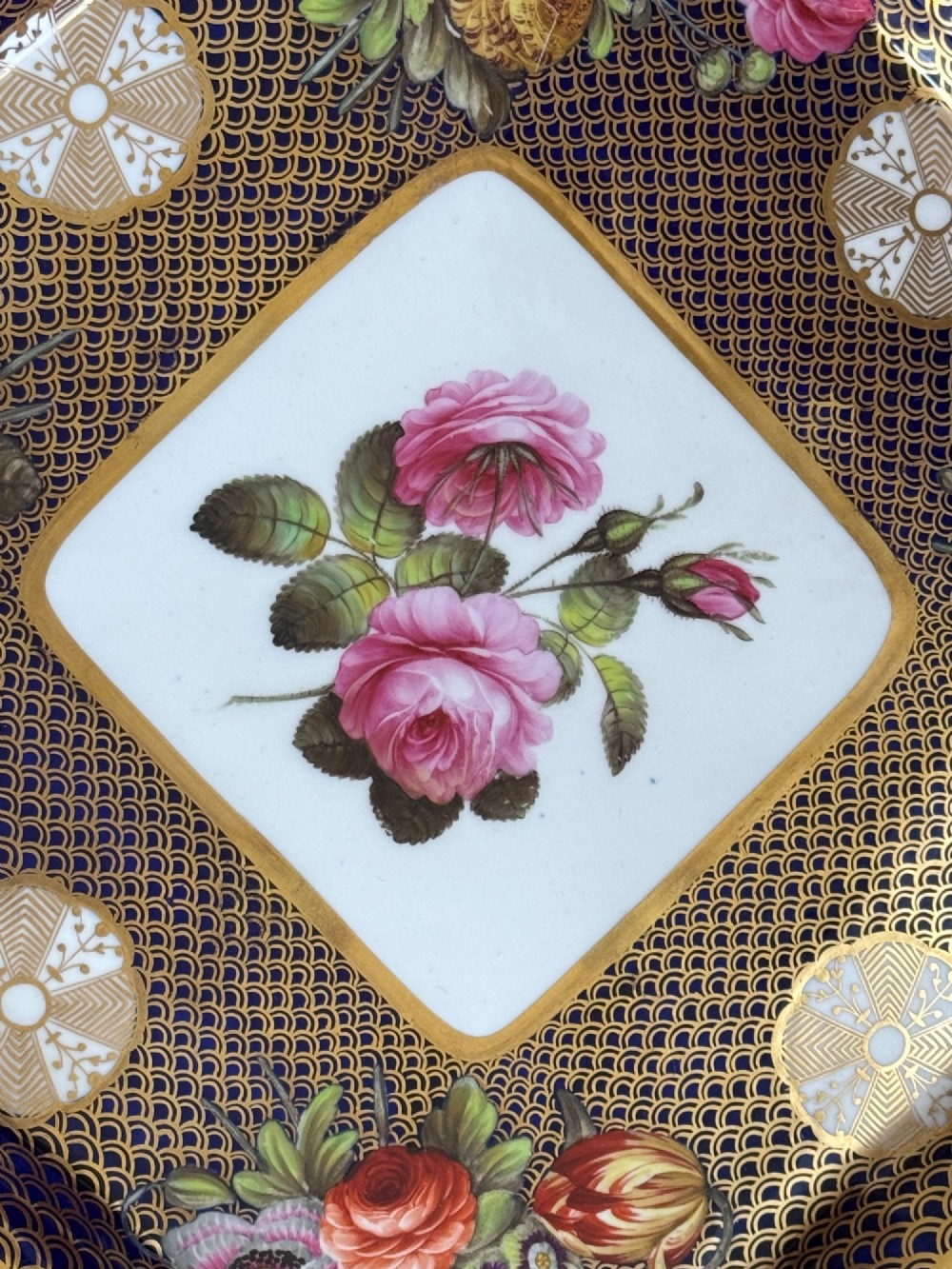 A square Regency porcelain tray featuring hand-painted floral bouquets, an intricate gilt scale pattern over a cobalt blue ground, and a central white reserve with pink roses. View VI