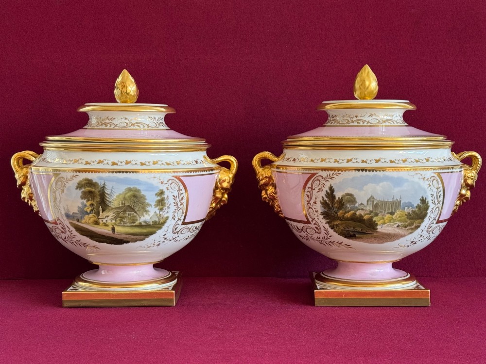 A pair of antique Regency porcelain ice pails featuring pink and white grounds, hand-painted landscape scenes, gilded lion mask handles, and pinecone finials. View III