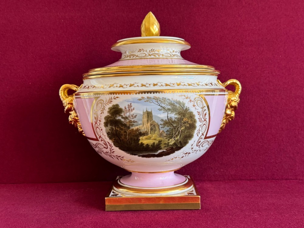A pair of antique Regency porcelain ice pails featuring pink and white grounds, hand-painted landscape scenes, gilded lion mask handles, and pinecone finials. View VI