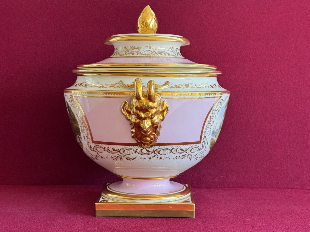 A pair of antique Regency porcelain ice pails featuring pink and white grounds, hand-painted landscape scenes, gilded lion mask handles, and pinecone finials. View IX