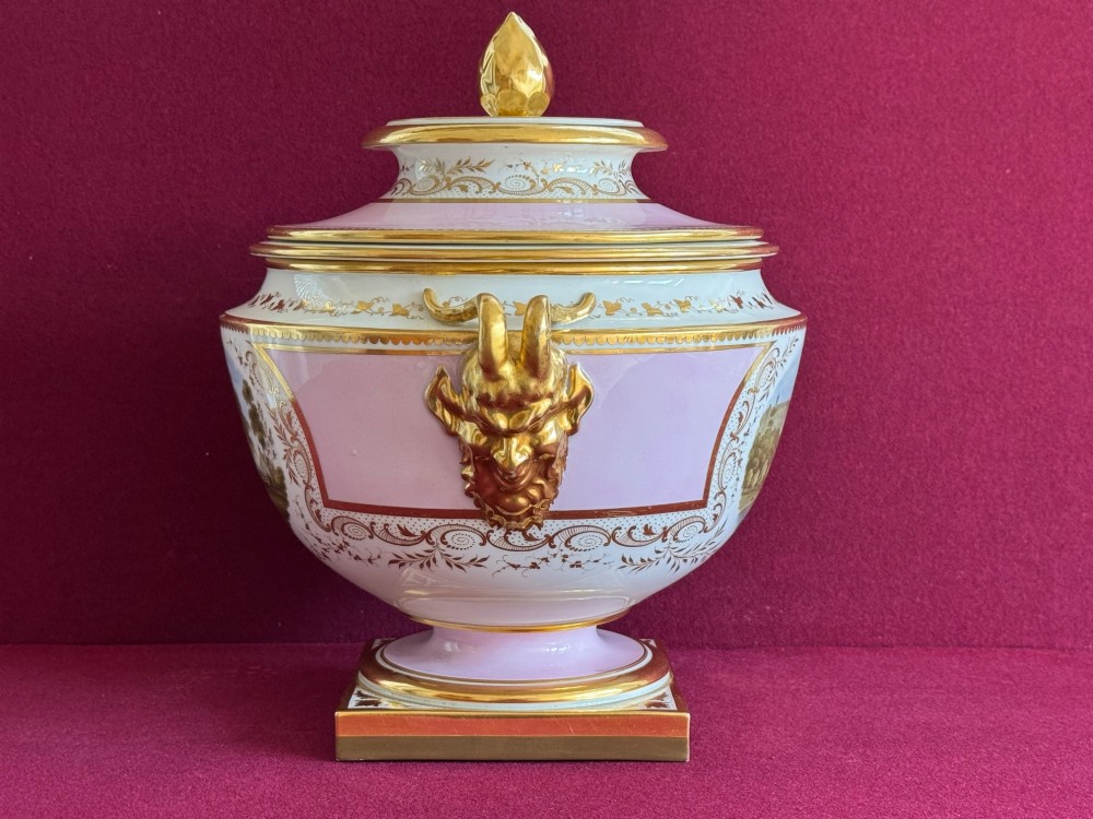 A pair of antique Regency porcelain ice pails featuring pink and white grounds, hand-painted landscape scenes, gilded lion mask handles, and pinecone finials. View XI