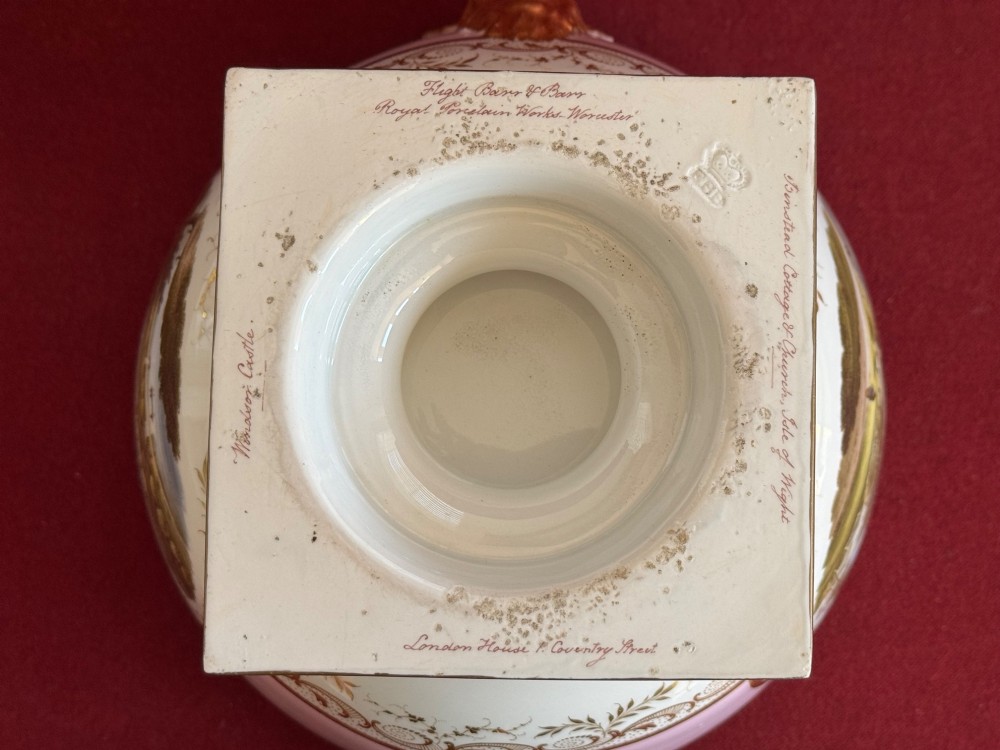 A pair of antique Regency porcelain ice pails featuring pink and white grounds, hand-painted landscape scenes, gilded lion mask handles, and pinecone finials. View XII