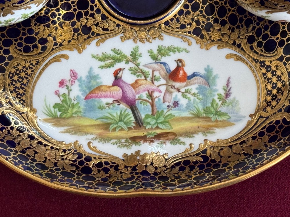 An oval cobalt blue porcelain inkstand decorated with gold honeycomb diapering, hand-painted bird cartouches, and two covered inkwells with gilt branch handles. View II