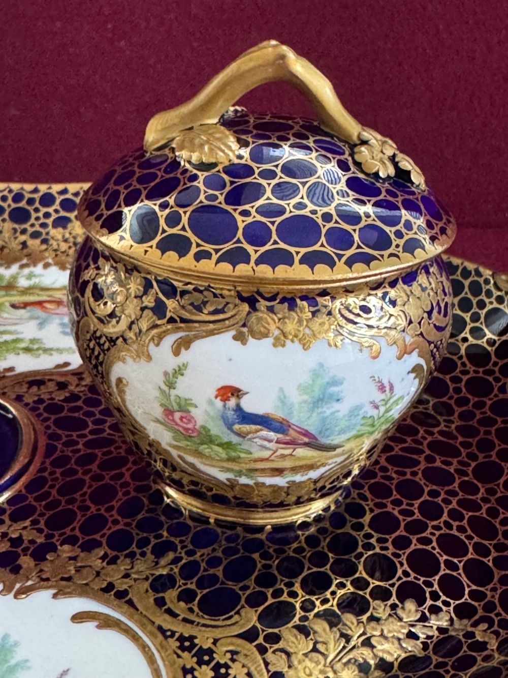 An oval cobalt blue porcelain inkstand decorated with gold honeycomb diapering, hand-painted bird cartouches, and two covered inkwells with gilt branch handles. View V