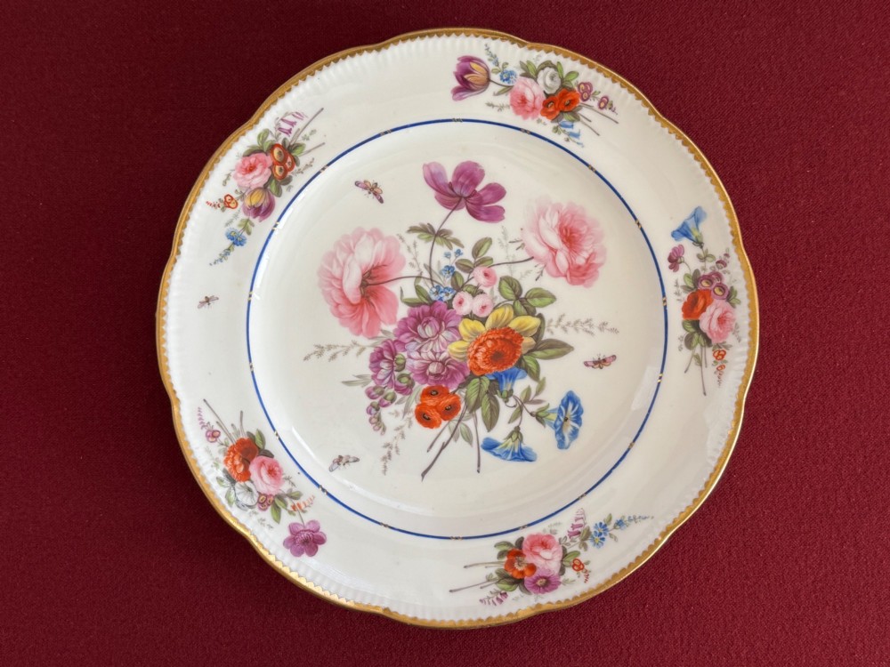 A pair of circular white Regency porcelain plates with lobed gilded rims and hand-painted floral bouquets at the centre and border. View II