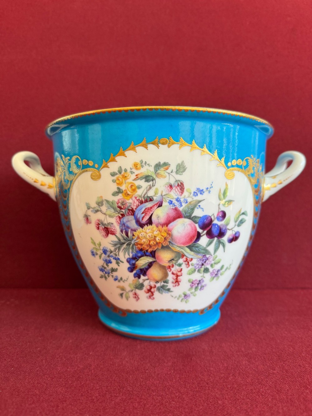 A pair of turquoise porcelain bottle coolers featuring hand-painted fruit cartouches framed by gilded scrollwork and twin handles. View II