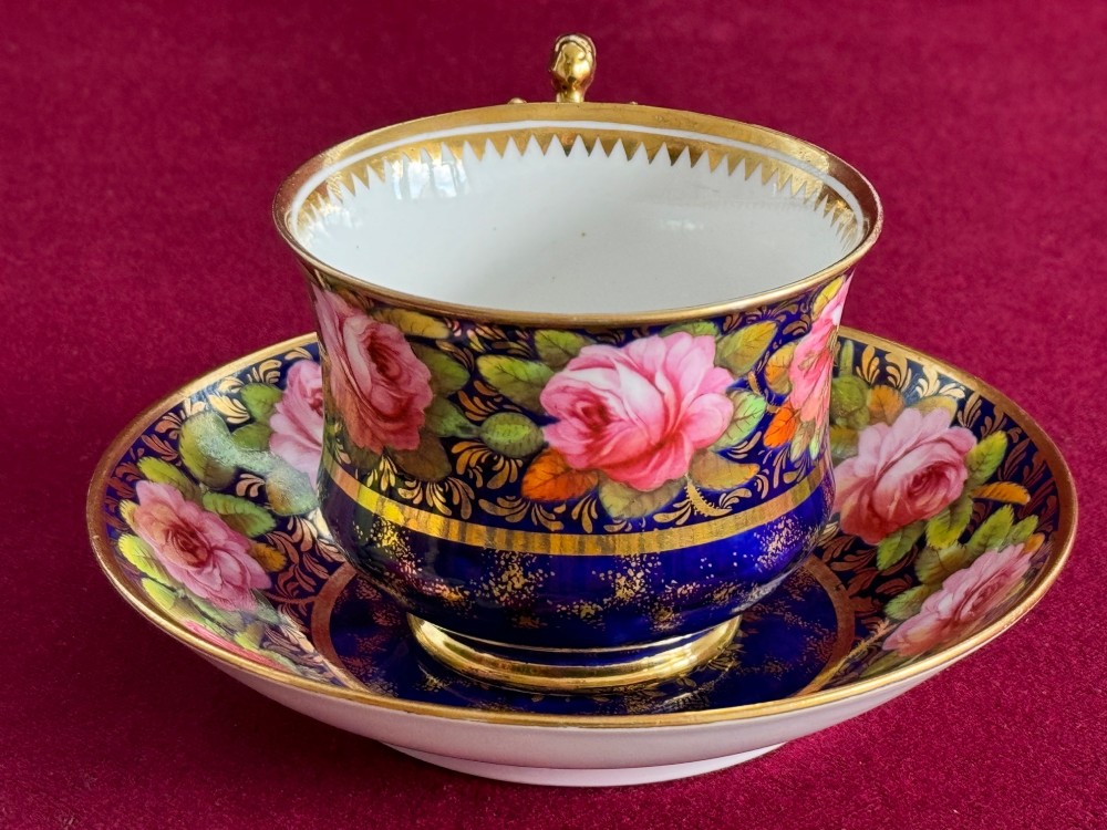 An antique Regency period Spode porcelain teacup and saucer decorated with hand-painted pink roses, cobalt blue ground, gold leaf gilding, and a gilded figural handle. View II