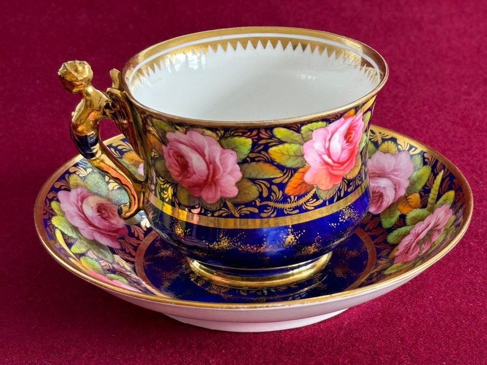 An antique Regency period Spode porcelain teacup and saucer decorated with hand-painted pink roses, cobalt blue ground, gold leaf gilding, and a gilded figural handle. View III