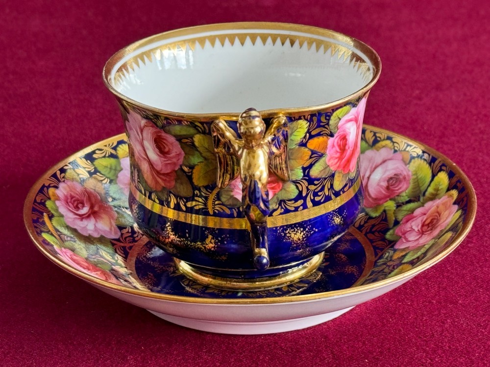 An antique Regency period Spode porcelain teacup and saucer decorated with hand-painted pink roses, cobalt blue ground, gold leaf gilding, and a gilded figural handle. View IV
