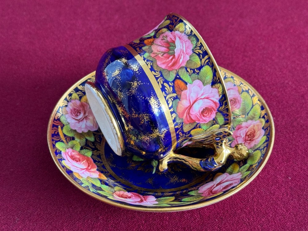 An antique Regency period Spode porcelain teacup and saucer decorated with hand-painted pink roses, cobalt blue ground, gold leaf gilding, and a gilded figural handle. View V