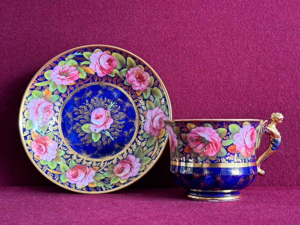 An antique Regency period Spode porcelain teacup and saucer decorated with hand-painted pink roses, cobalt blue ground, gold leaf gilding, and a gilded figural handle. View VI