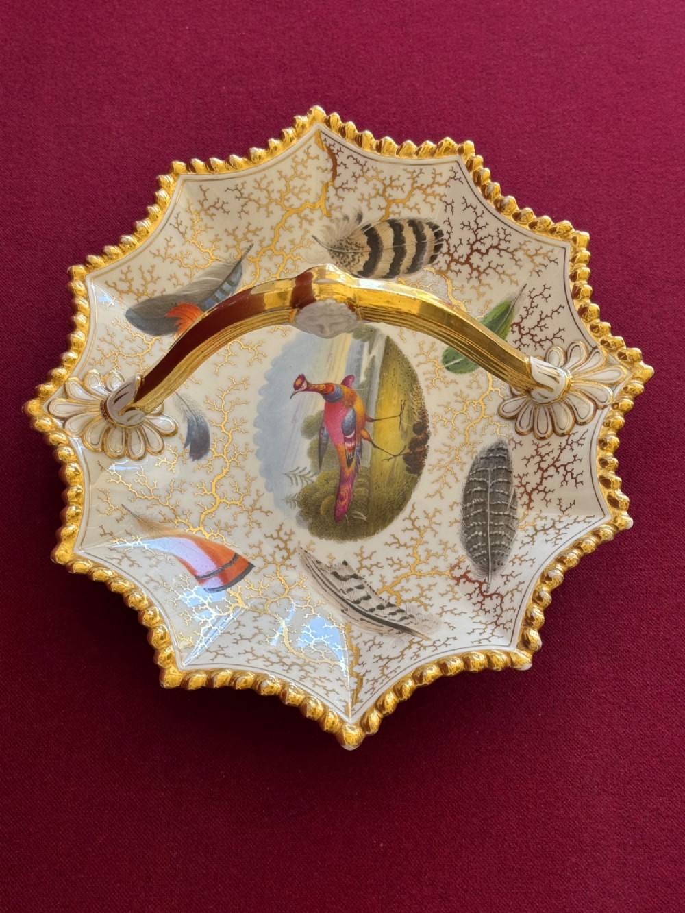 An early 19th-century shaped Regency porcelain basket featuring an overhead gilt handle, a central hand-painted bird vignette, feather studies, and gold seaweed detailing on a white ground. View V