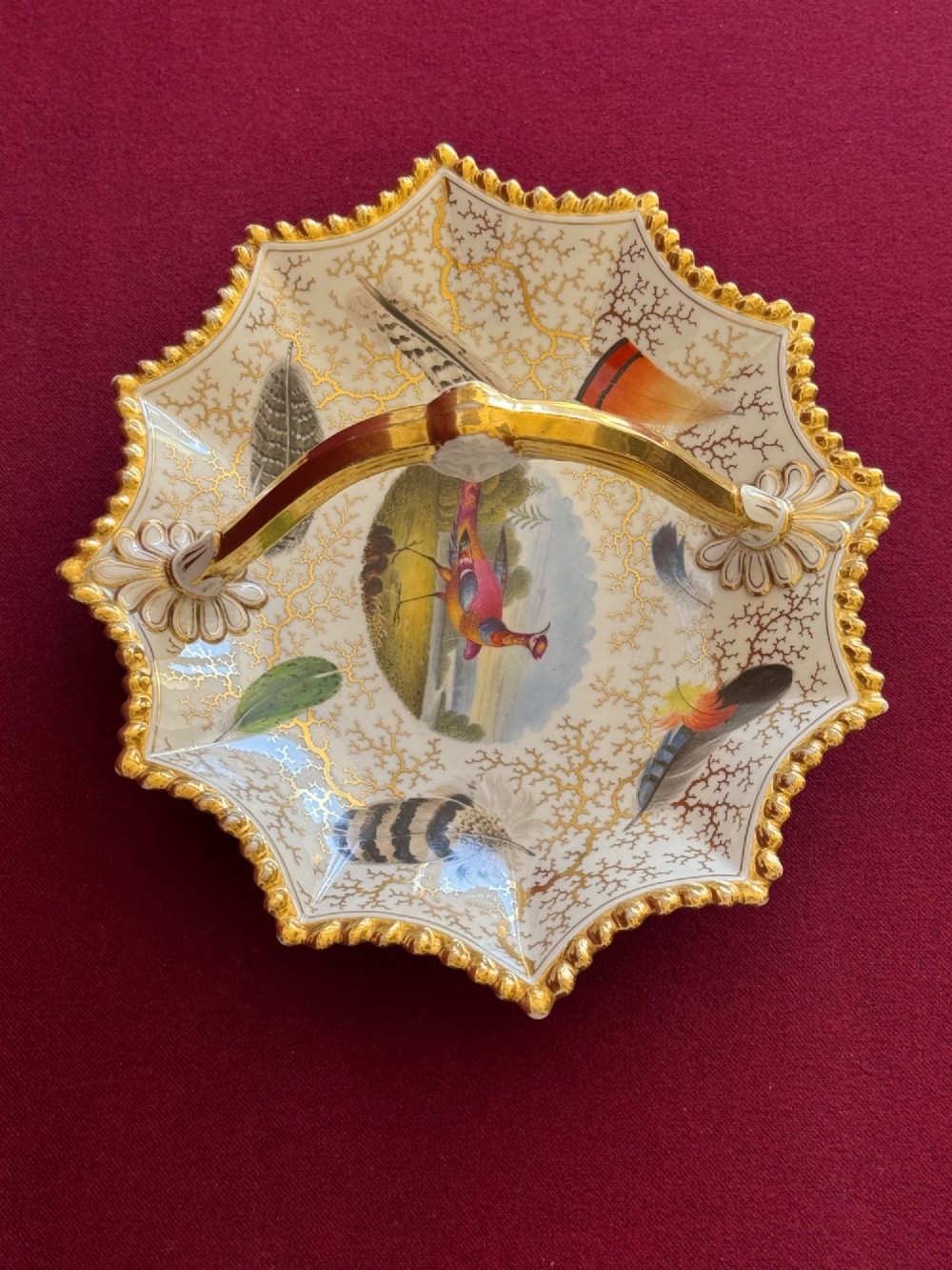 An early 19th-century shaped Regency porcelain basket featuring an overhead gilt handle, a central hand-painted bird vignette, feather studies, and gold seaweed detailing on a white ground. View VI