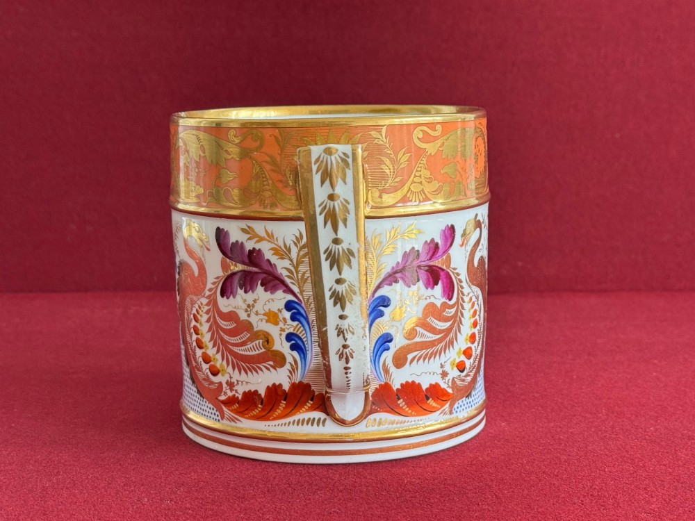 A cylindrical Regency period Derby porcelain porter mug decorated with hand-painted bird motifs, gold leaf foliage, an orange top border, and an angular gilded handle. View V