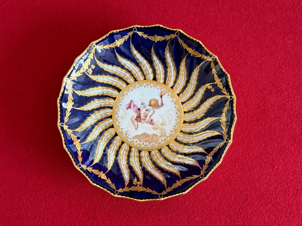 An 18th-century cobalt blue and gilded soft-paste porcelain chocolate cup with lid alongside a matching saucer decorated with a painted central cherub motif. View III
