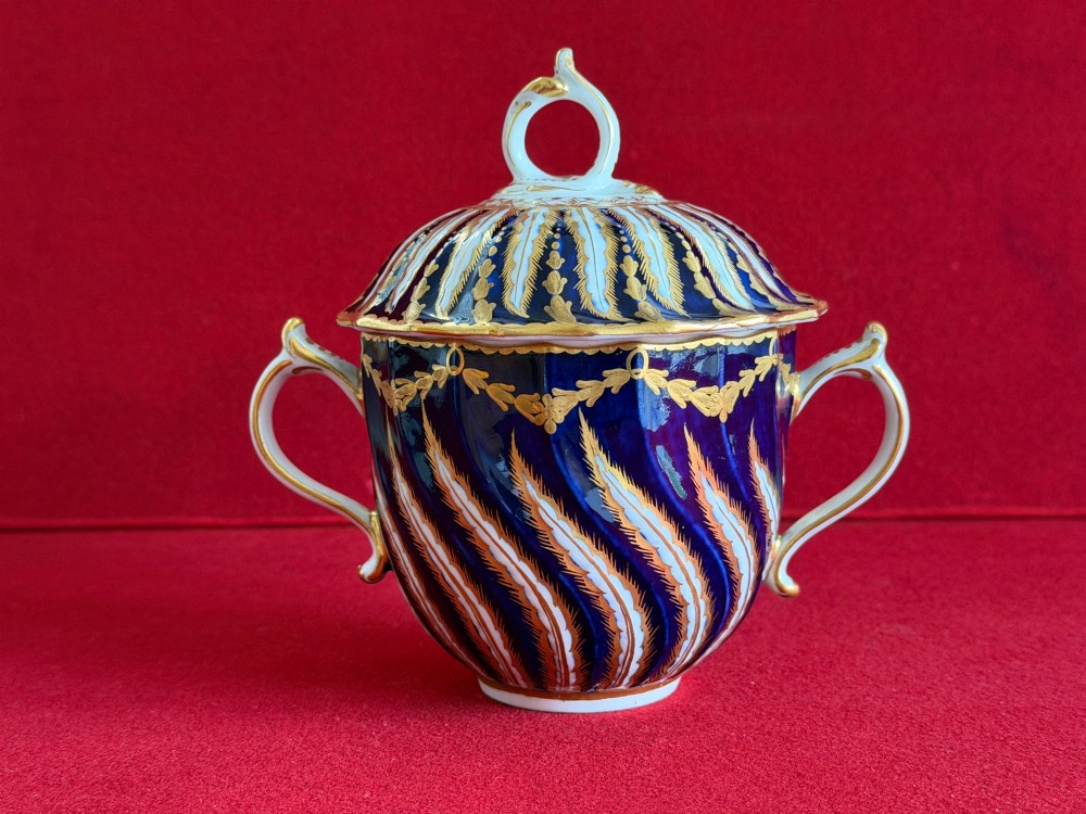 An 18th-century cobalt blue and gilded soft-paste porcelain chocolate cup with lid alongside a matching saucer decorated with a painted central cherub motif. View V