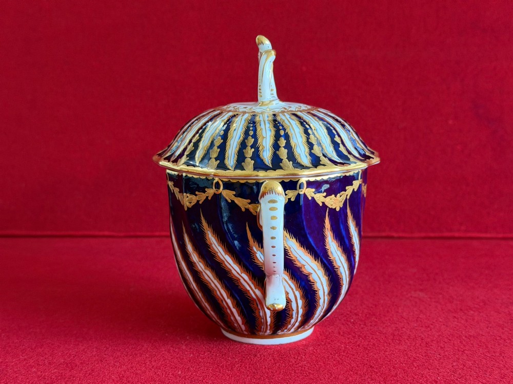 An 18th-century cobalt blue and gilded soft-paste porcelain chocolate cup with lid alongside a matching saucer decorated with a painted central cherub motif. View VII