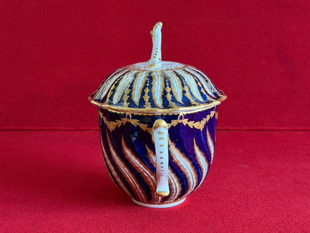 An 18th-century cobalt blue and gilded soft-paste porcelain chocolate cup with lid alongside a matching saucer decorated with a painted central cherub motif. View IX