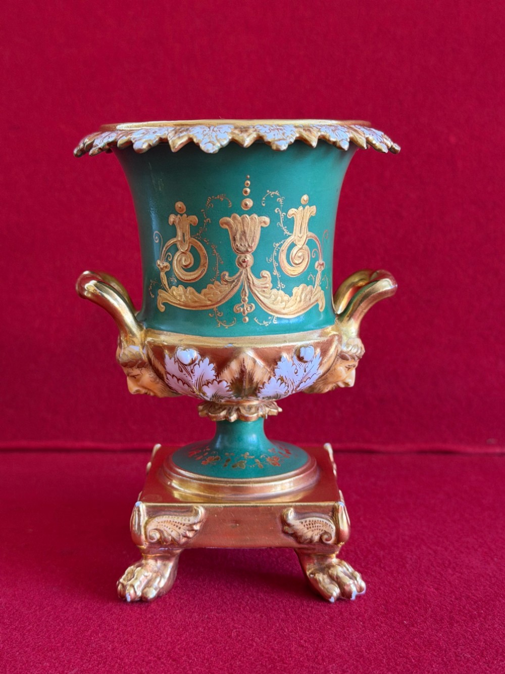 A three-piece antique porcelain garniture set featuring green and gold gilded urns with hand-painted floral panels on pedestal bases with paw feet. View V