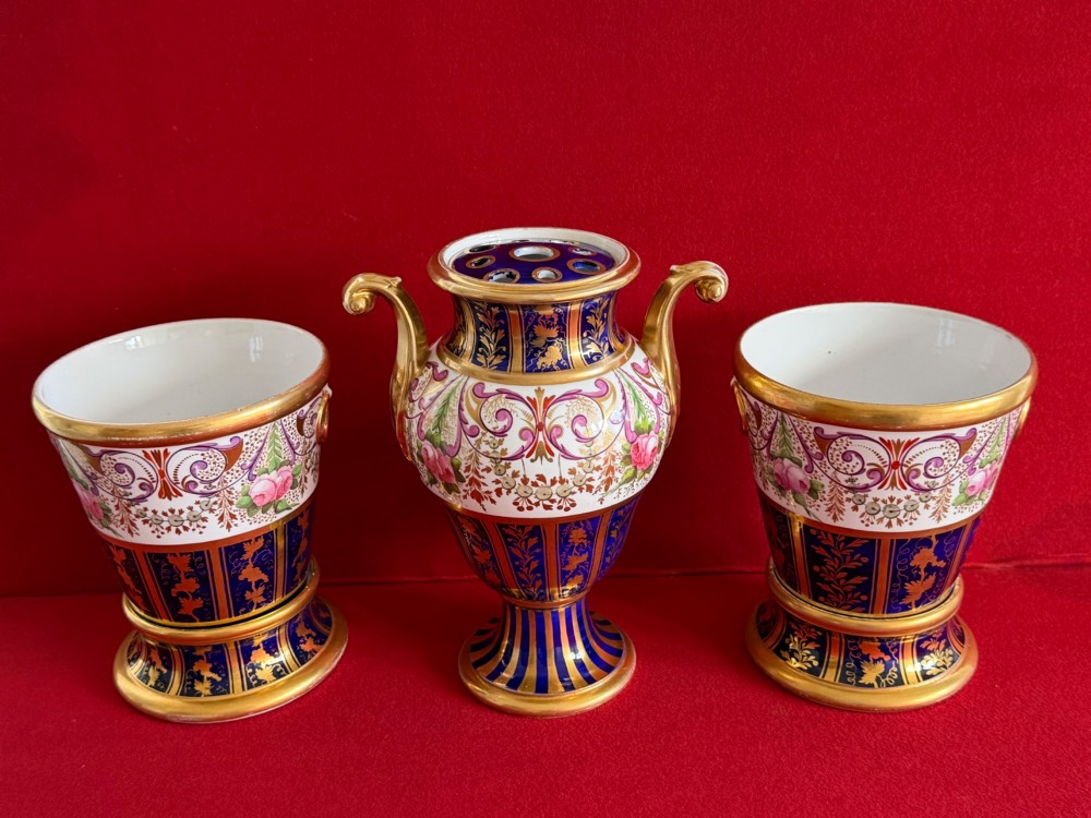 A three-piece English Regency Spode porcelain garniture featuring a central twin-handled urn flanked by two beaker-shaped vases decorated with cobalt blue panels, hand-painted pink floral motifs, and detailed gilt scrollwork. View II
