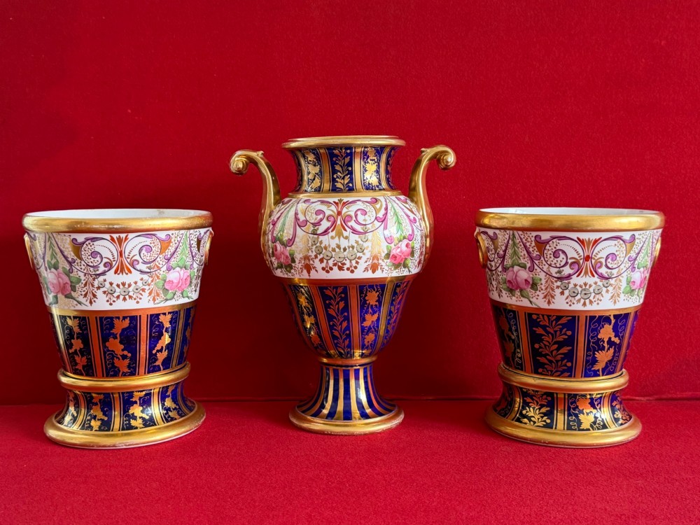 A three-piece English Regency Spode porcelain garniture featuring a central twin-handled urn flanked by two beaker-shaped vases decorated with cobalt blue panels, hand-painted pink floral motifs, and detailed gilt scrollwork. View III