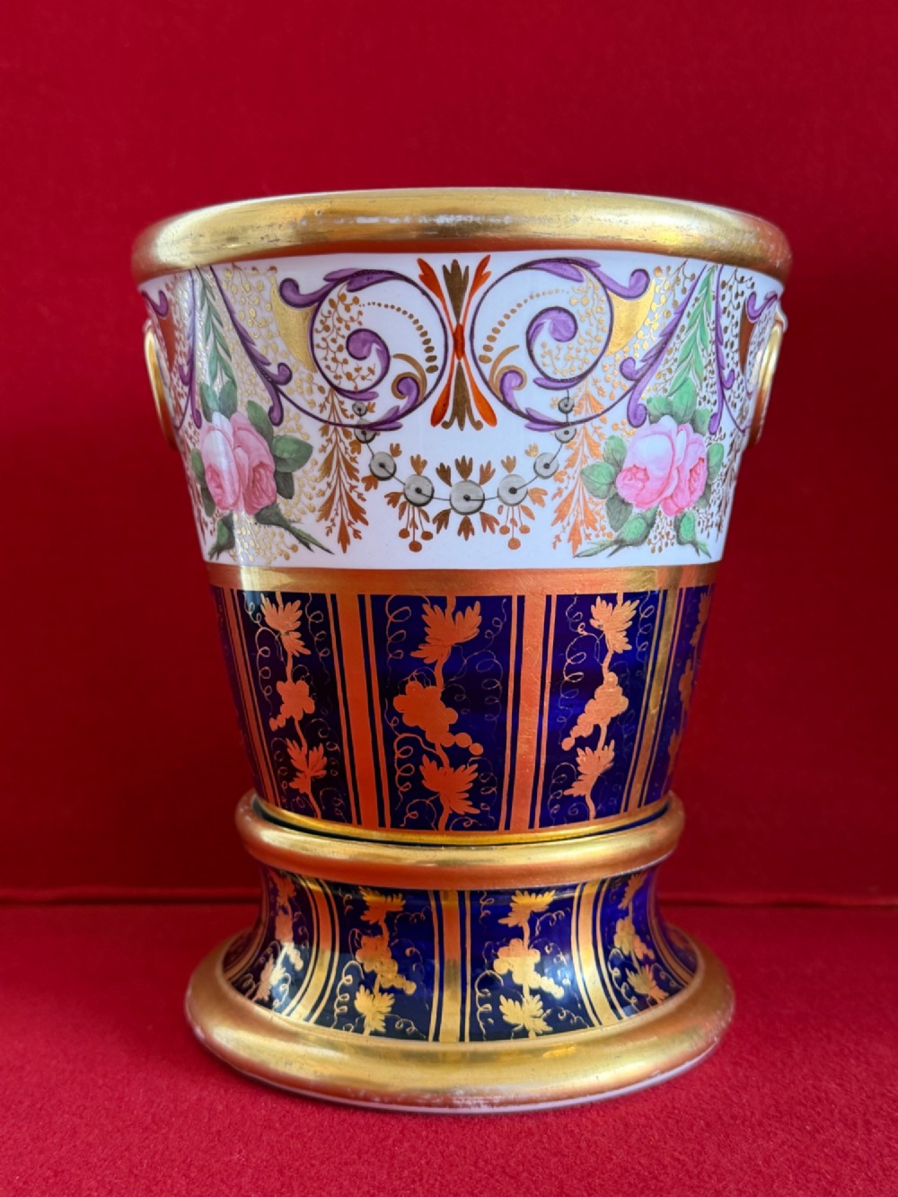 A three-piece English Regency Spode porcelain garniture featuring a central twin-handled urn flanked by two beaker-shaped vases decorated with cobalt blue panels, hand-painted pink floral motifs, and detailed gilt scrollwork. View V